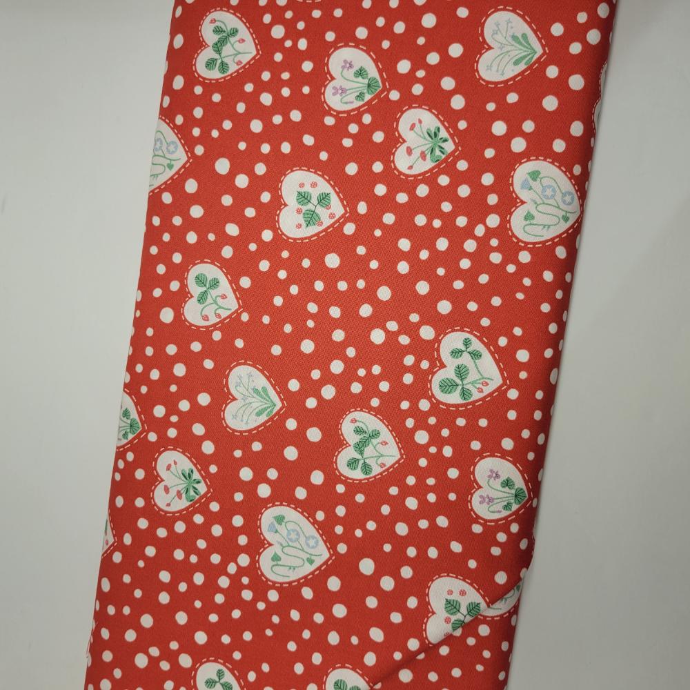 Red fabric with white polka dots and green heart patterns on a plain background