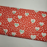 Red fabric with white polka dots and green heart patterns on a plain background