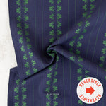 A close-up of a navy blue fabric with vertical green stripes and repeating green floral motifs, draped to show its texture and pattern. A white circular sticker with a red arrow reads 'REVERSIBLE' is placed in the bottom right corner, and the brand name 'RABLBISM' is printed near the bottom center.