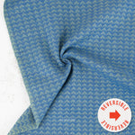 A close-up of a blue woven fabric with a repeating chevron pattern, draped to show its texture and reversible side, with a circular 'REVERSIBLE' badge in the bottom right corner.