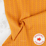 A close-up of folded orange fabric with a repeating small geometric pattern, shown on a light textured surface. A white circular badge in the lower right says 'REVERSIBLE' with a red arrow, and a small 'PABLEISM' mark appears near the bottom center.