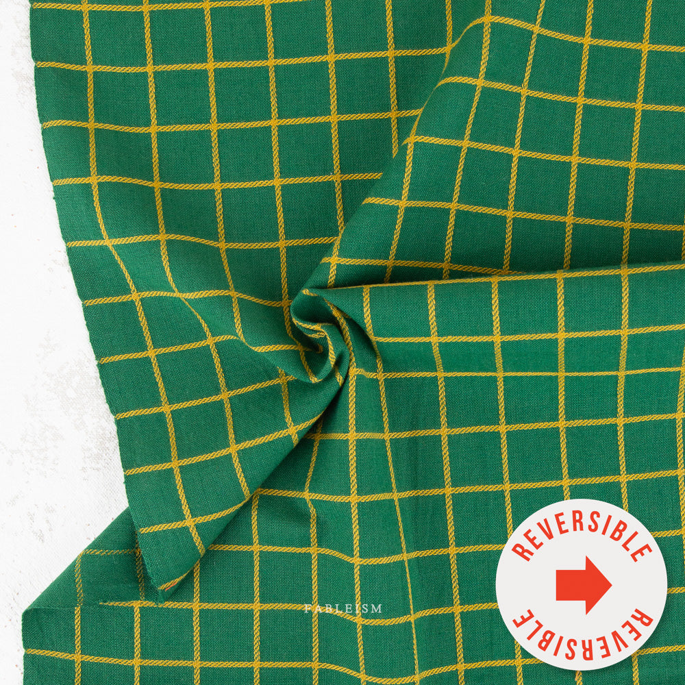 Green fabric with a yellow grid pattern, draped to show its texture and reversible design, with a circular badge indicating 'REVERSIBLE'.