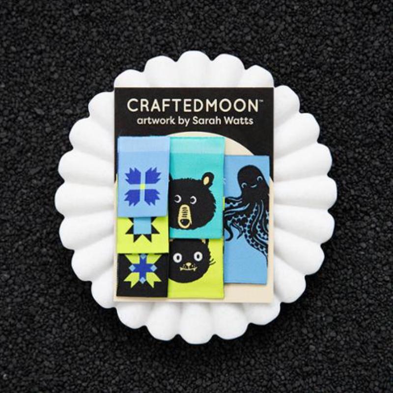 Product packaging with 'Crafted Moon' branding and artwork by Sarah Watts on a black background.