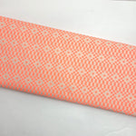 A close-up of a folded fabric or material sample with a repeating geometric pattern in coral pink and off-white on a plain white background.