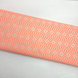 A close-up of a folded fabric or material sample with a repeating geometric pattern in coral pink and off-white on a plain white background.