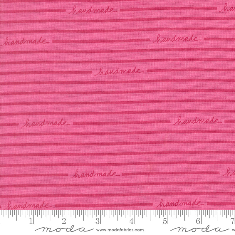 Pink fabric with 'handmade' text and Moda label, featuring a ruler for scale.