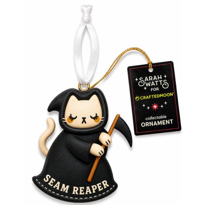 A collectible Christmas ornament shaped like a cat dressed as a grim reaper, wearing a black robe and holding a scythe. The ornament has a white hanging ribbon and a black product tag that reads 'Sarah Watts for Craftedmoon collectable Ornament'.