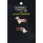 Two enamel lapel pins shaped like dachshunds, decorated with colorful quilted patterns, displayed on a black card that reads 'Sarah Watts for Crafted Moon'.