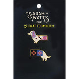 Two enamel lapel pins shaped like dachshunds, decorated with colorful quilted patterns, displayed on a black card that reads 'Sarah Watts for Crafted Moon'.