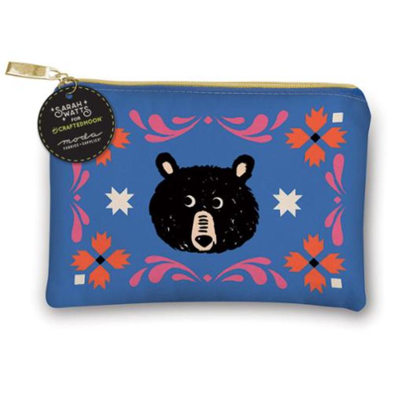 A blue zippered pouch featuring a black bear face illustration and pink, orange, and white decorative motifs, with a gold zipper and a hanging circular tag reading Sarah + Wyatt x Crafted Moon.